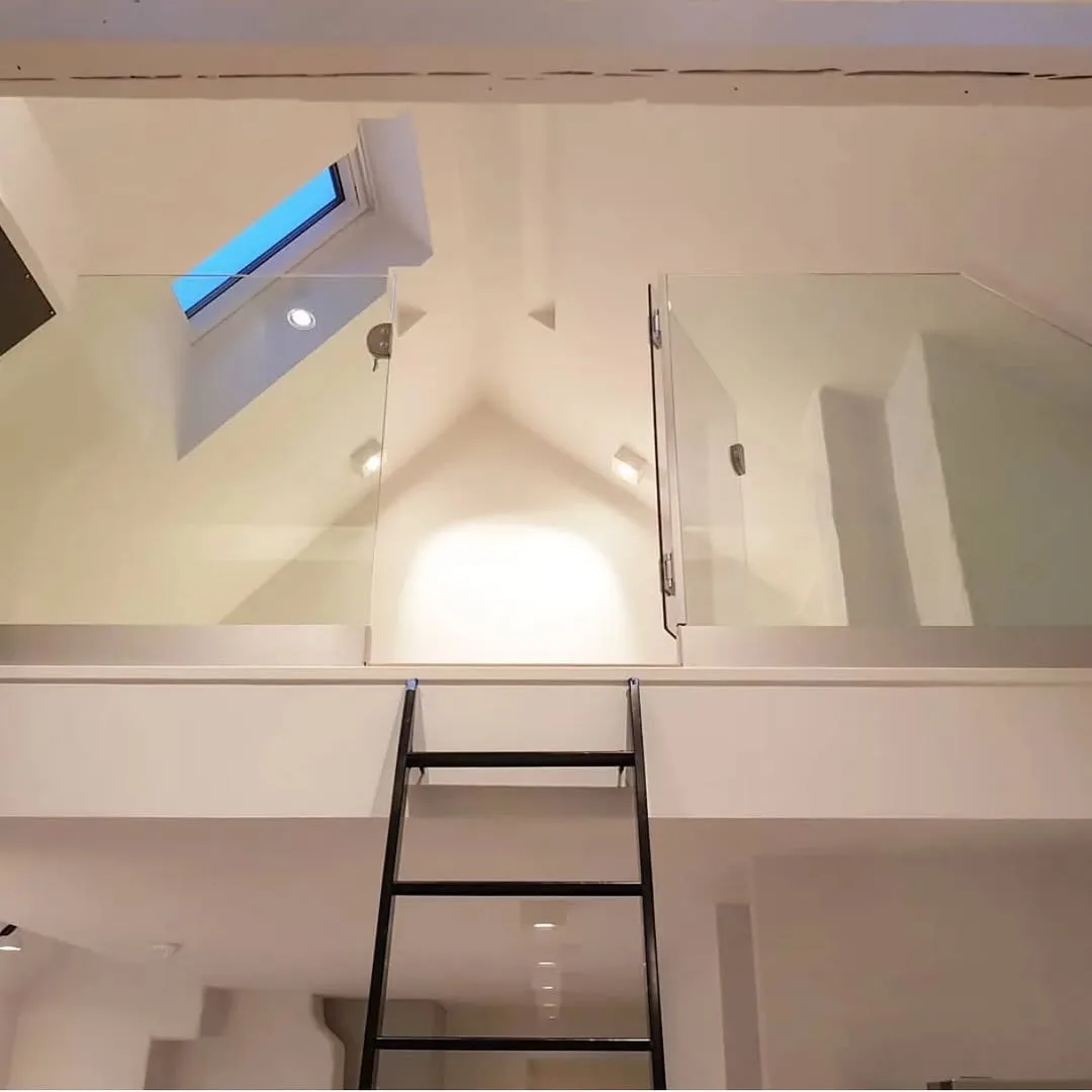 Altillo con barandilla de cristal, escalera metálica negra y ventana de cubierta en reforma integral de vivienda