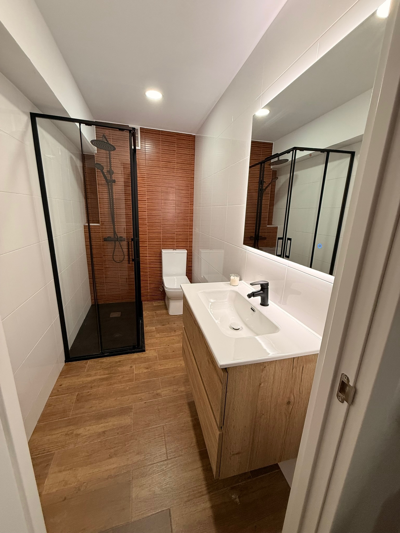 Reforma de baño completo con mueble de madera, ducha con grifo negro mate y suelo imitación madera — Grupo Cárdenas Rojas Valencia
