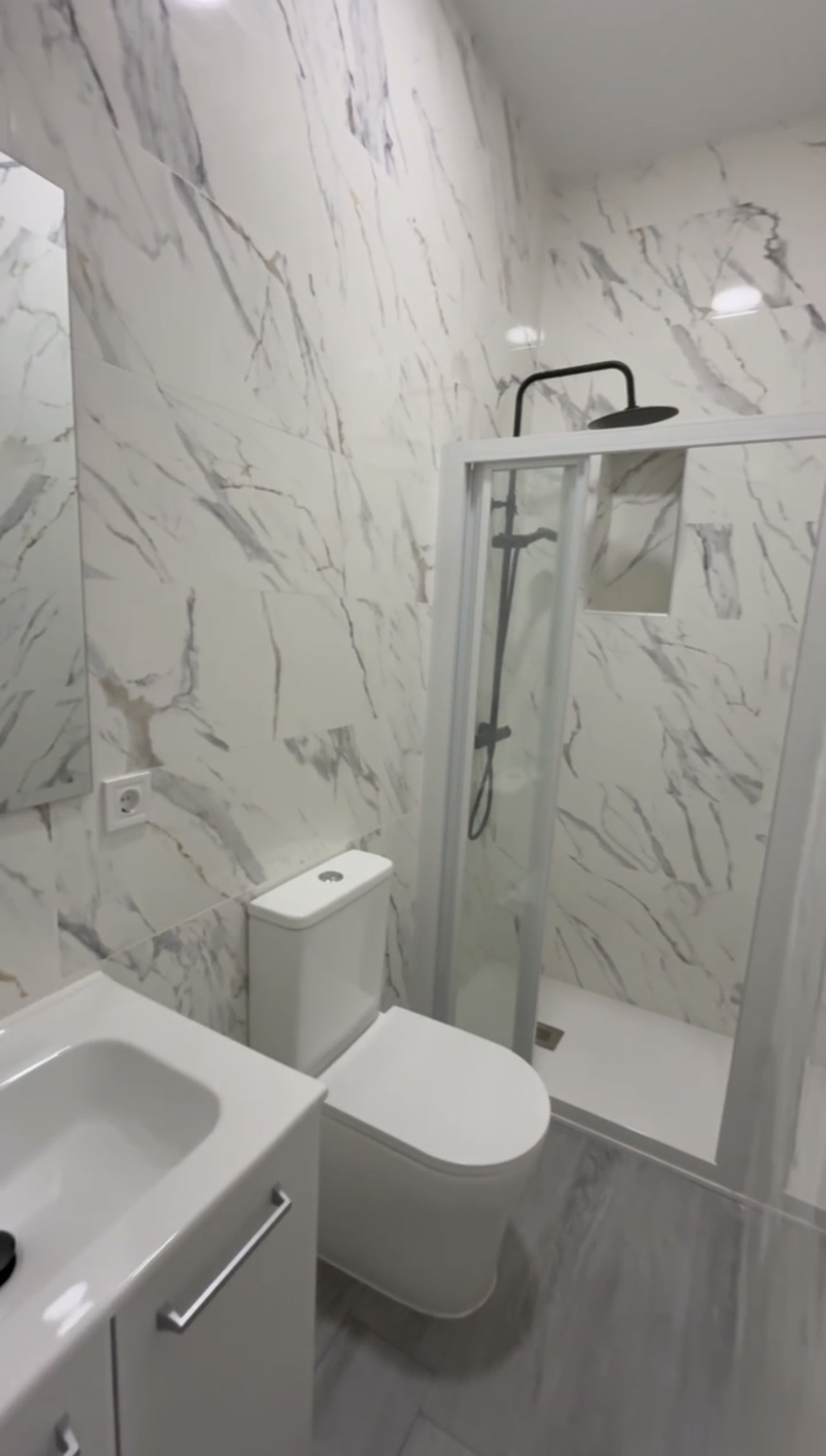 Baño reformado con azulejos efecto mármol blanco y ducha tipo rainfall con grifo negro mate — Grupo Cárdenas Rojas Valencia