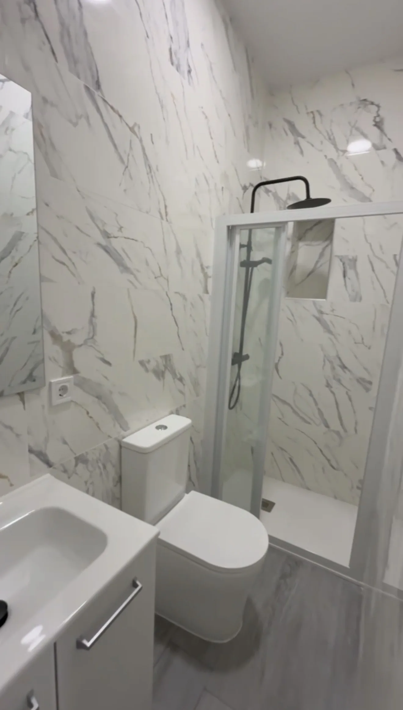 Baño reformado con azulejos efecto mármol blanco y ducha tipo rainfall con grifo negro mate — Grupo Cárdenas Rojas Valencia