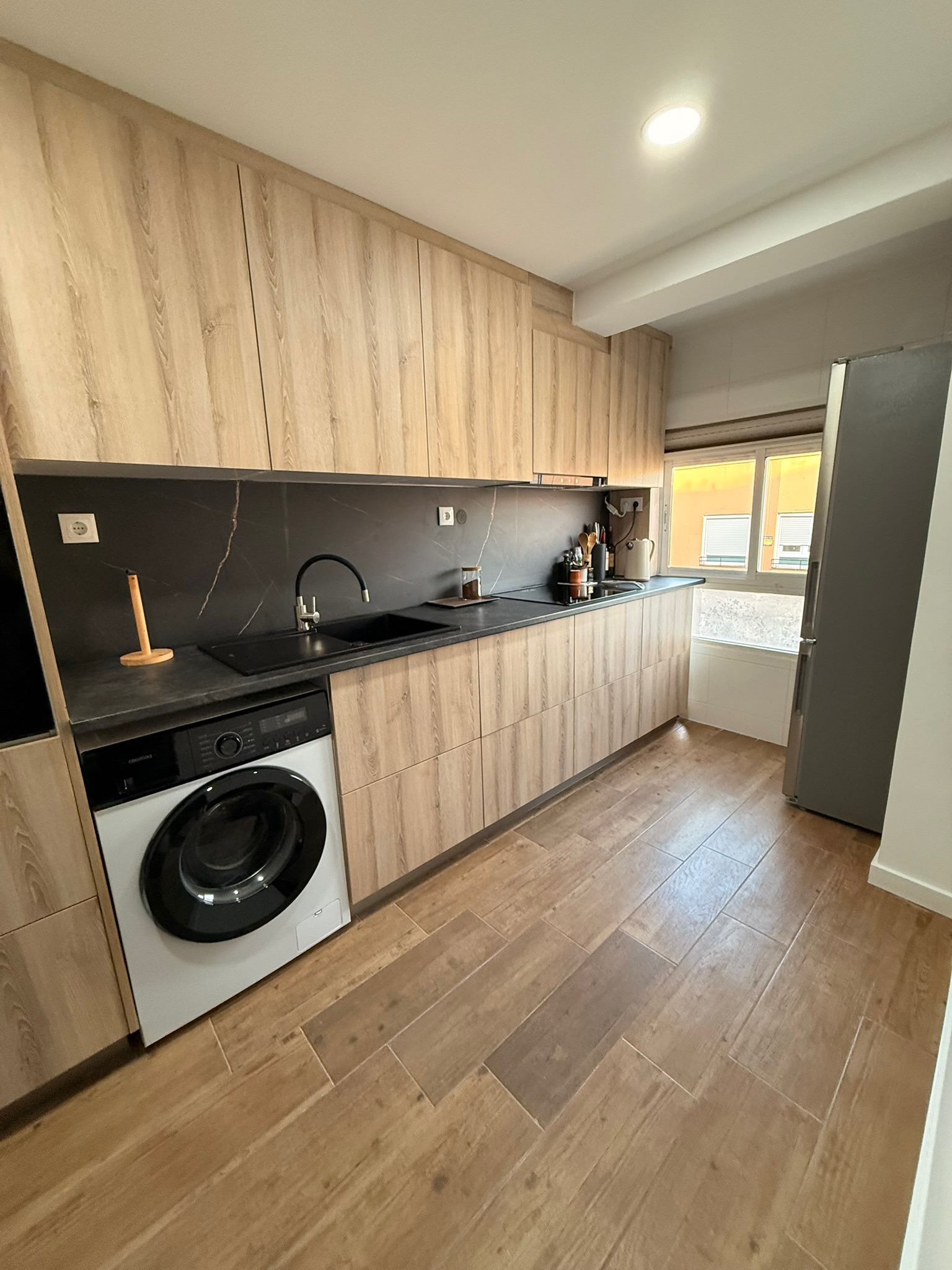 Cocina reformada con encimera negra efecto piedra, fregadero integrado negro y muebles de madera clara — Grupo Cárdenas Rojas Valencia