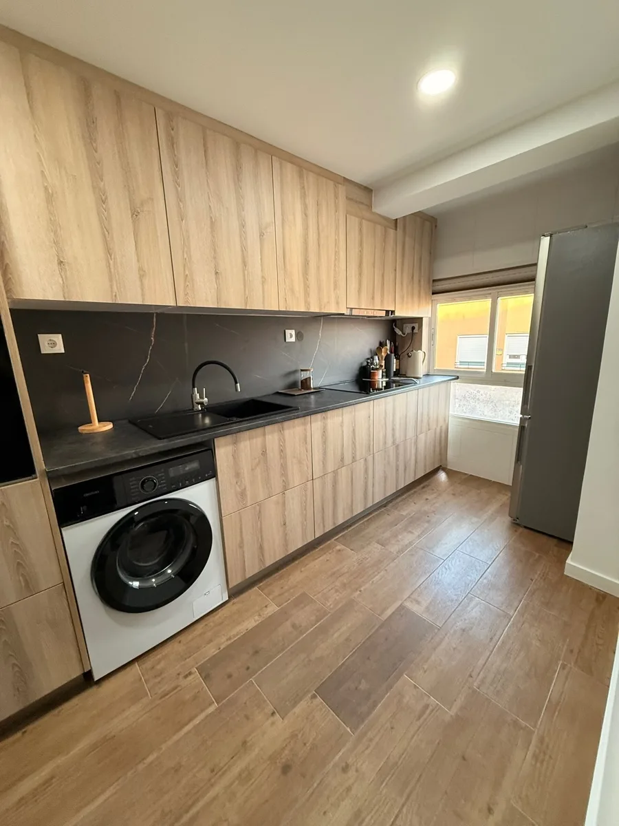 Cocina reformada con encimera negra efecto piedra, fregadero integrado negro y muebles de madera clara — Grupo Cárdenas Rojas Valencia