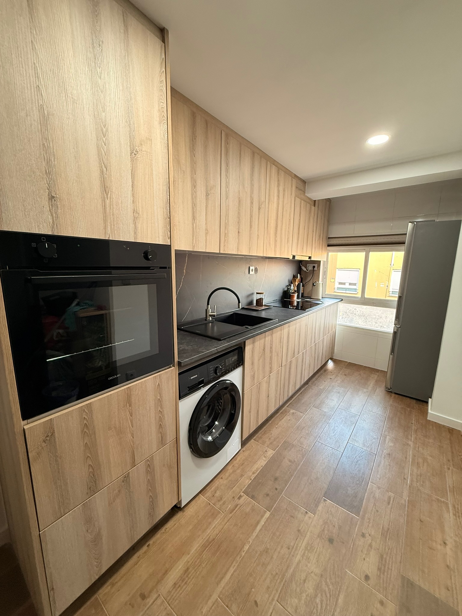 Reforma de cocina moderna con muebles de madera de suelo a techo, horno negro integrado y encimera oscura — Grupo Cárdenas Rojas Valencia