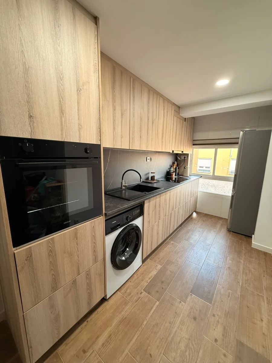 Reforma de cocina moderna con muebles de madera de suelo a techo, horno negro integrado y encimera oscura — Grupo Cárdenas Rojas Valencia